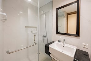 A modern bathroom with a glass-enclosed shower, a white sink, and a large mirror with a dark frame. - Serene 1Br With Nature View At Apartment Lavaya Nusa Dua Bali (Bali)