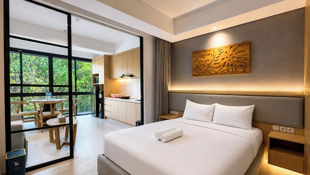 A modern hotel room with a large bed, a dining area, and a view of greenery. - Serene 1Br With Nature View At Apartment Lavaya Nusa Dua Bali (Bali)