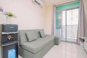 A modern living room with a grey sofa, a water dispenser, and a view of a balcony. - Enjoy Living 1Br Apartment At Pejaten Park Residence (Jakarta)
