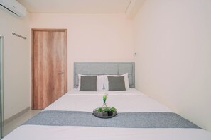 A hotel room with a bed, a wooden door, and a wall-mounted air conditioner. - Enjoy Living 1Br Apartment At Pejaten Park Residence (Jakarta)