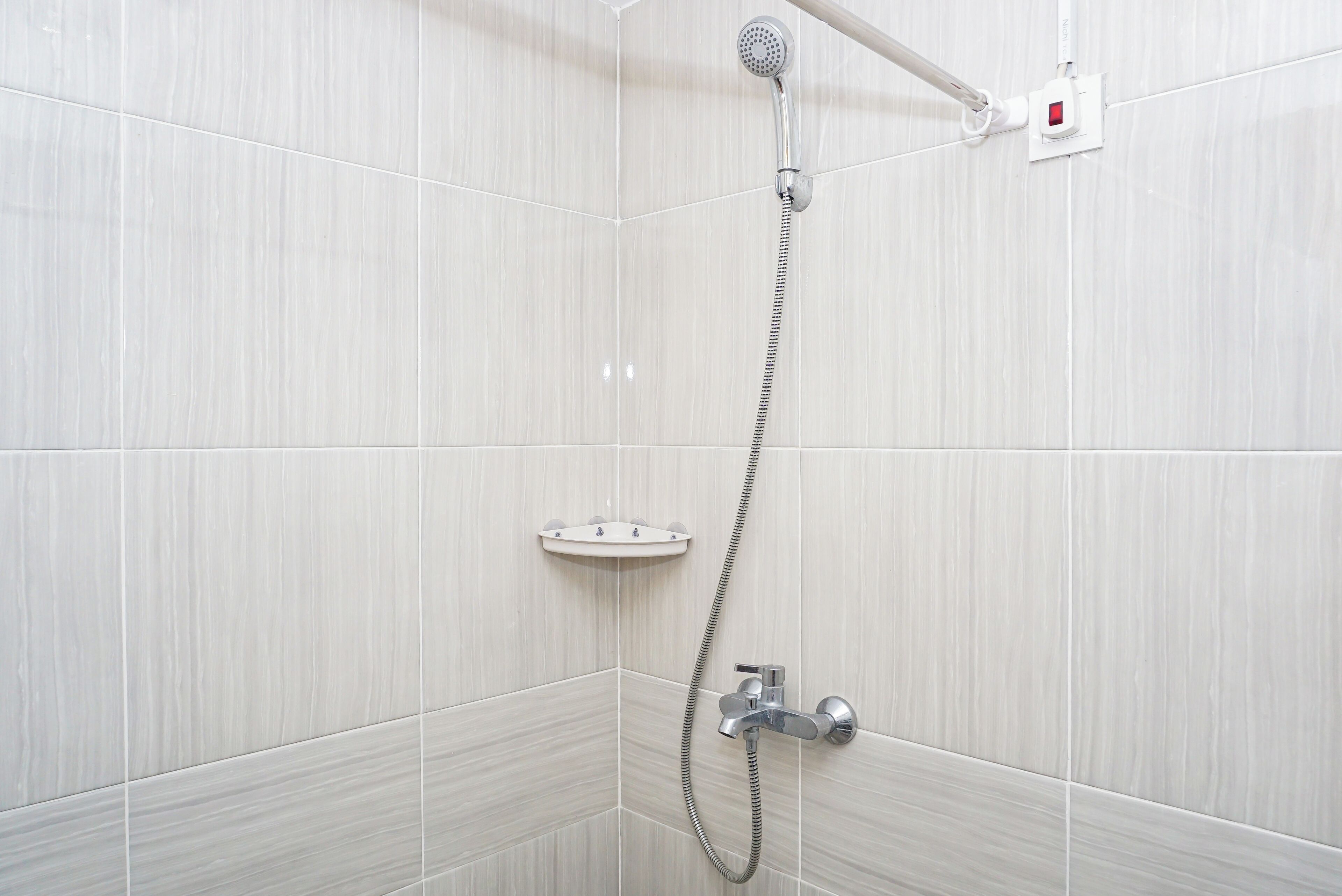 Eine Dusche mit Duschbrause, Bedienfeld an der Wand und Duschschlauch.