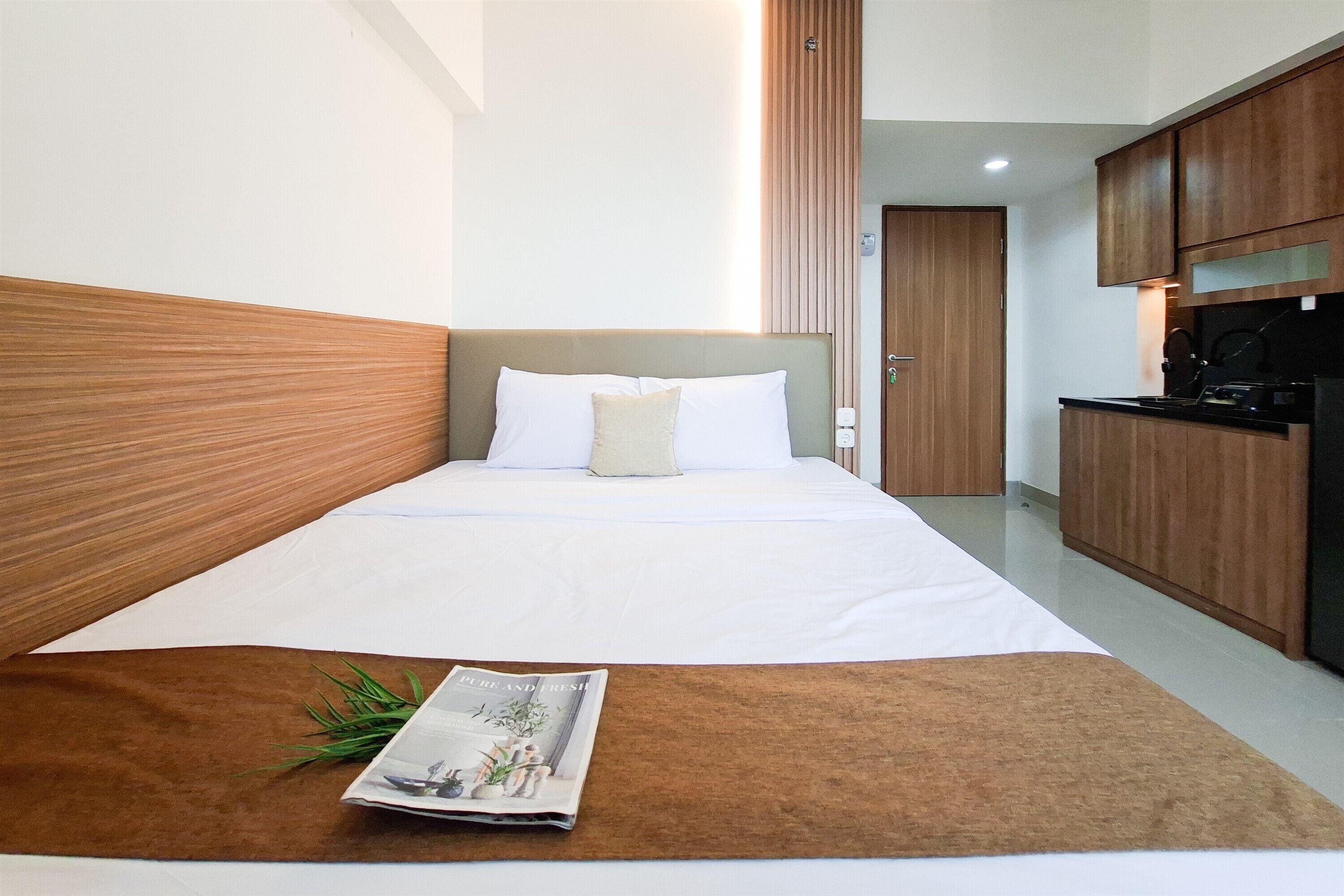 A hotel room with a bed, a magazine on the bed, a kitchen area, and a door.