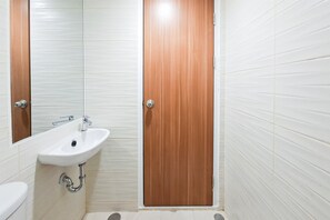 Ein Badezimmer mit einem weißen Waschbecken, einem Spiegel und einer Holztür.