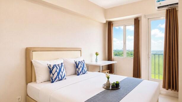 Una habitación de hotel con cama, una mesita, una ventana con cortinas y un equipo de aire acondicionado.