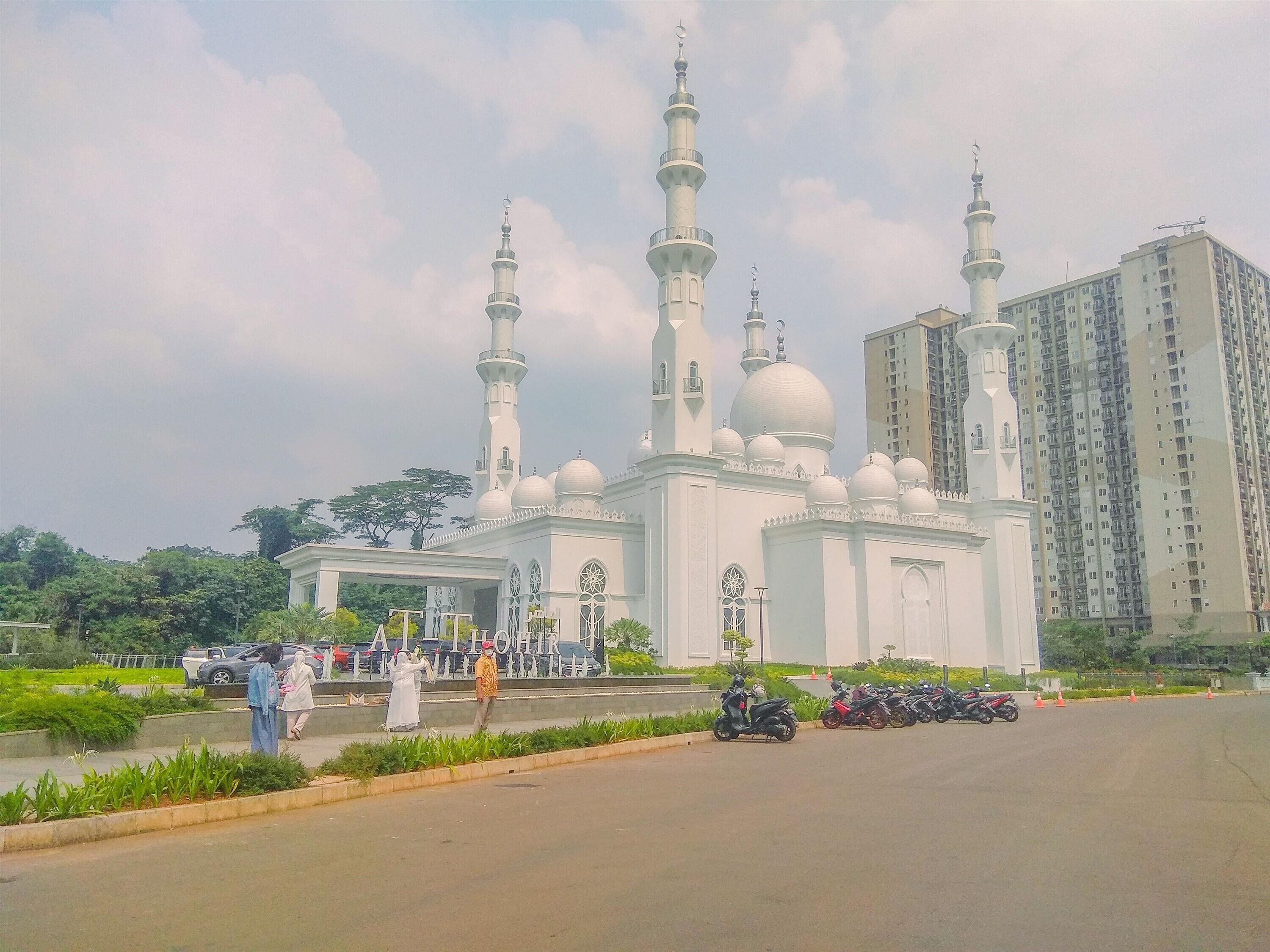 A mosque with multiple minarets and domes, surrounded by greenery and a parking area with motorcycles.