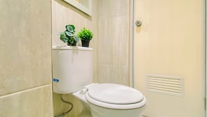 Un inodoro con tanque y tapa blancos, una planta pequeña en maceta encima y un respiradero en la pared.