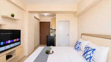 Habitación de hotel con cama, televisor sobre un soporte, una planta pequeña y una puerta que da al baño.