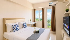 Una habitación de hotel con cama, televisor, ventana con cortinas y aire acondicionado.
