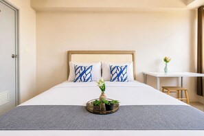 Quarto de hotel com cama, uma mesinha, uma cadeira e um vaso com flores.