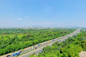 Autoestrada com várias faixas e veículos, rodeada por vegetação densa e paisagem urbana ao longe.