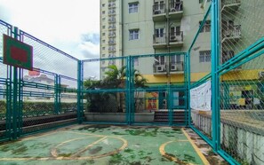 An outdoor basketball court enclosed by a green fence, with a building in the background. - Chic Minimalist Studio At Apartment Suites @Metro (Bandung)