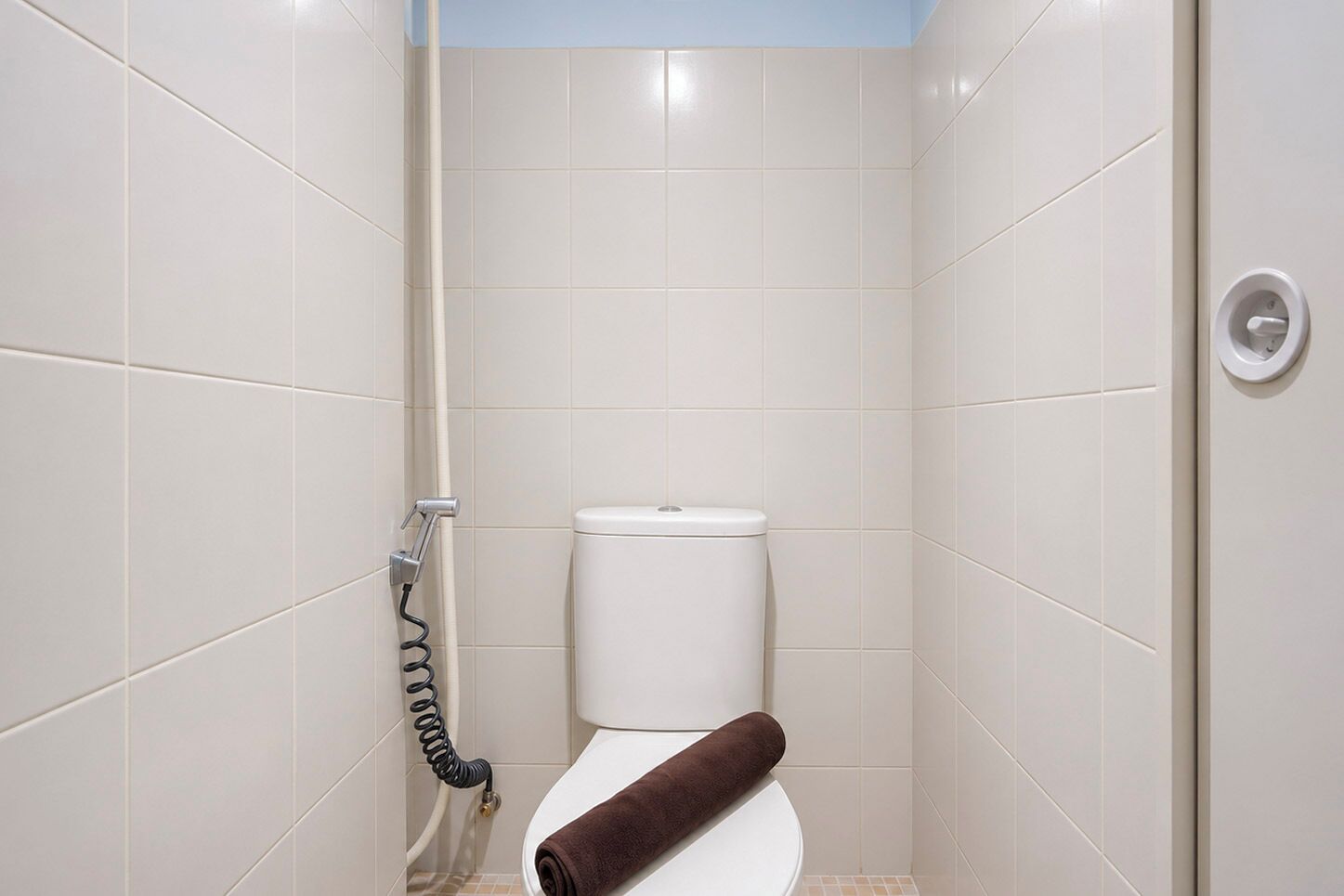 A small, enclosed bathroom with a toilet, a towel, and a shower hose.