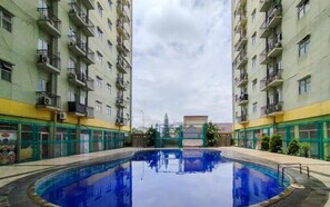 A swimming pool surrounded by high-rise residential buildings with balconies and air conditioning units. - Chic Minimalist Studio At Apartment Suites @Metro (Bandung)