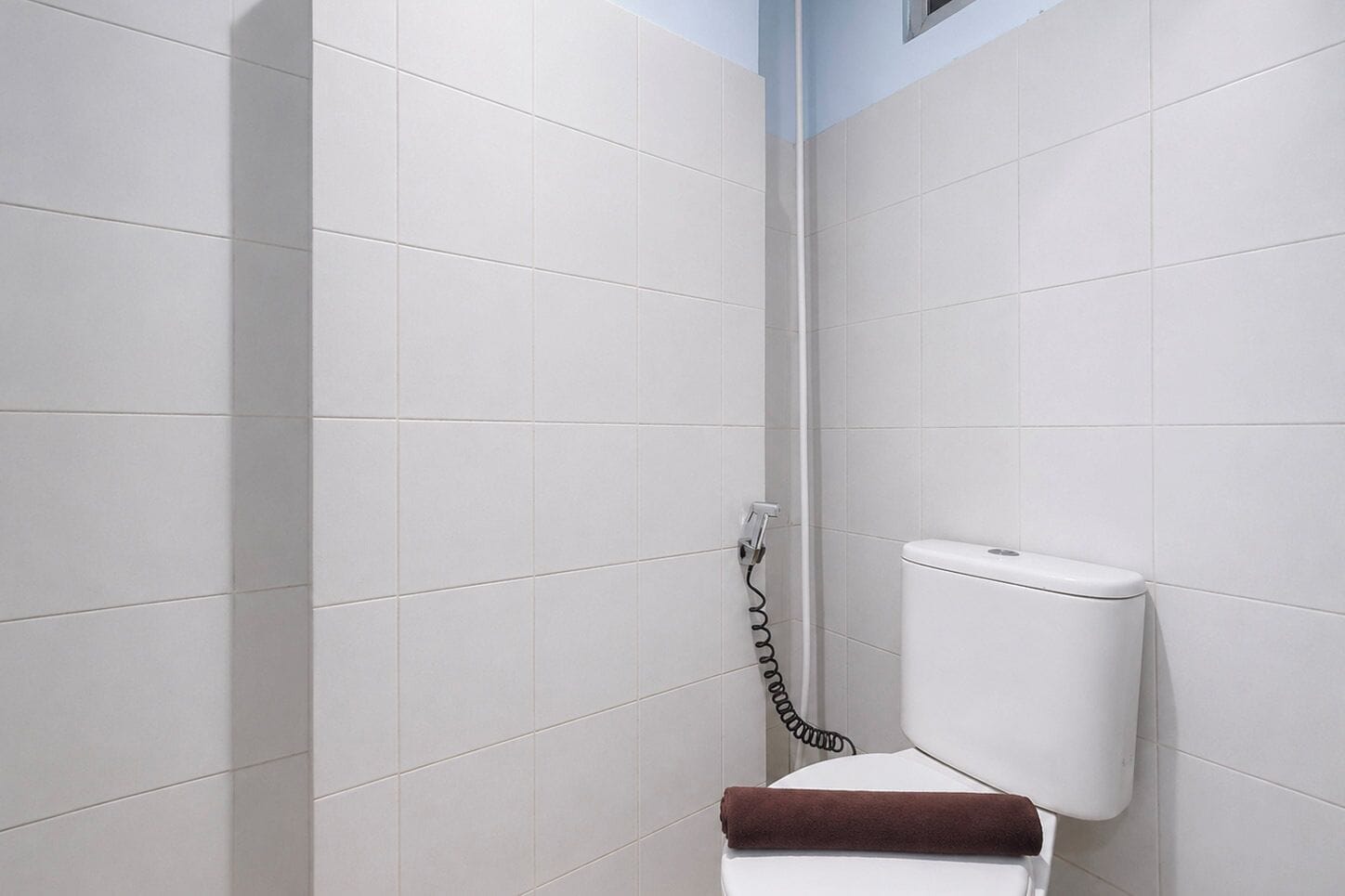 Baño con paredes de azulejos blancos, inodoro blanco y zona de ducha.
