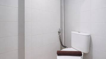 Baño con paredes de azulejos blancos, inodoro blanco y zona de ducha.