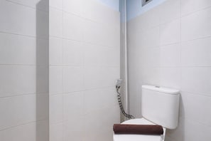 A bathroom with white tiled walls, a white toilet, and a shower area. - Chic Minimalist Studio At Apartment Suites @Metro (Bandung)