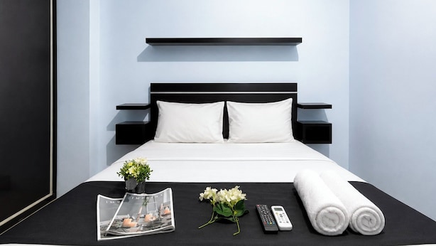 Ein modernes Hotelzimmer mit Bett, Nachttischen, einer Zeitschrift, einer Fernbedienung und einem zusammengerollten Handtuch.