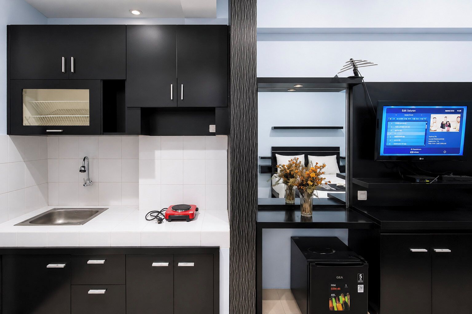 Una cocina moderna con armarios negros, un lavamanos de acero inoxidable, un electrodoméstico rojo y un televisor mostrando un programa.