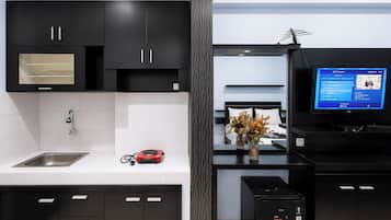 Una cocina moderna con armarios negros, un lavamanos de acero inoxidable, un electrodoméstico rojo y un televisor mostrando un programa.