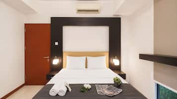 A hotel room with a bed, bedside tables, an air conditioning unit, a door, and a window.