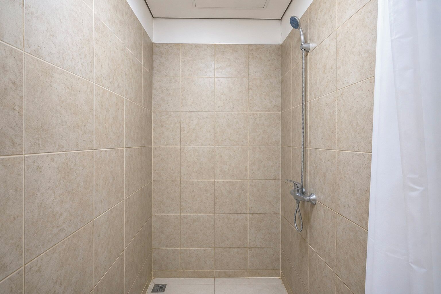 A small, tiled shower room with a showerhead and a curtain.