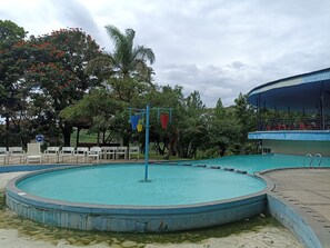 Ein runder Pool mit blauer Umrandung, umgeben von weißen Stühlen und einer überdachten Sitzgelegenheit.