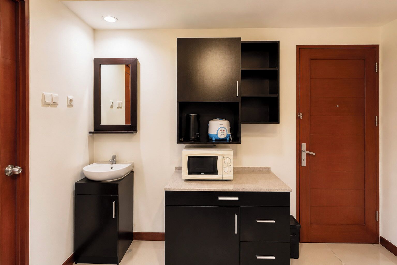 Un baño moderno con lavamanos, espejo, microondas y armarios negros.