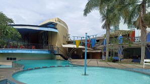 A swimming pool with a water slide, surrounded by buildings and palm trees. - Homey 2Br (No Kitchen) At Apartment Marbella Suites Dago Pakar Bandung (Bandung)