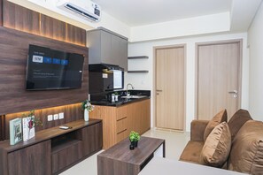 Een moderne woonkamer met een flatscreen televisie, houten kasten, een zwart aanrecht en een bruine bank.
