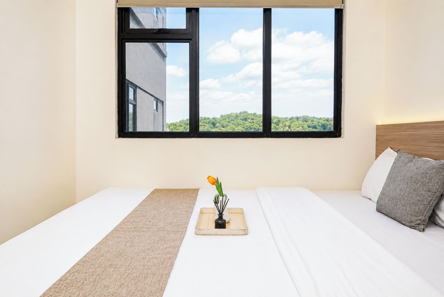 Habitación de hotel con cama, ventana que da a zonas verdes y mesita de noche con un florero.