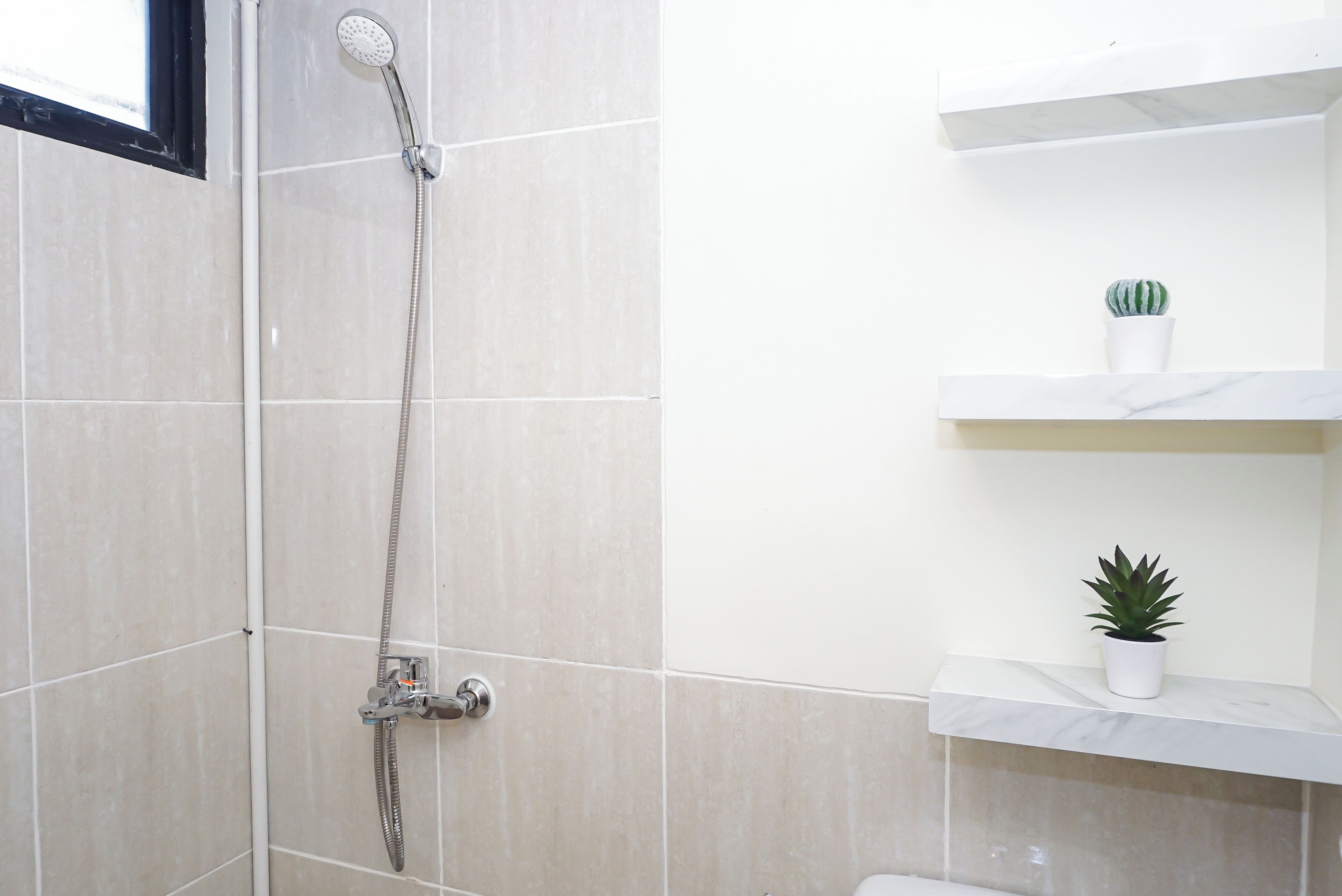A bathroom with a shower, tiled walls, and two potted plants on shelves.