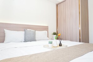 Een net opgemaakt bed met wit beddengoed, een hoofdbord en een nachtkastje met een vaas, een kleine plant en een kandelaar.
