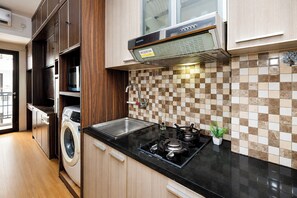 A compact kitchen with a washing machine, a stove, and a tiled backsplash. - Refined Studio At Apartment Tamansari Sudirman (Jakarta)
