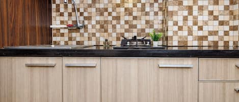 A kitchen with a checkered tile backsplash, a stainless steel faucet, a stove, and wooden cabinets.