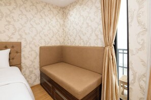 Ein Schlafzimmer mit einem Bett, einer Schlafcouch, einem Nachttisch aus Holz und einem Fenster mit Vorhängen.