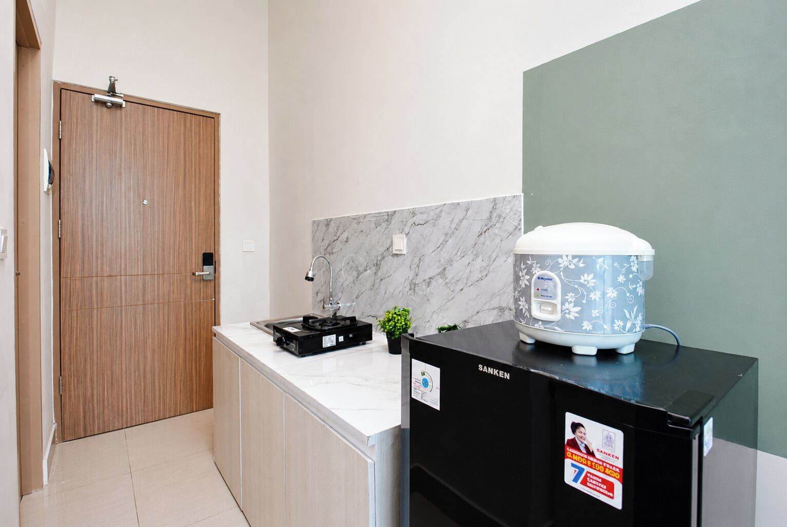 Una cocina compacta con protector contra salpicaduras de mármol, un refrigerador negro y una cocedora de arroz sobre la encimera.
