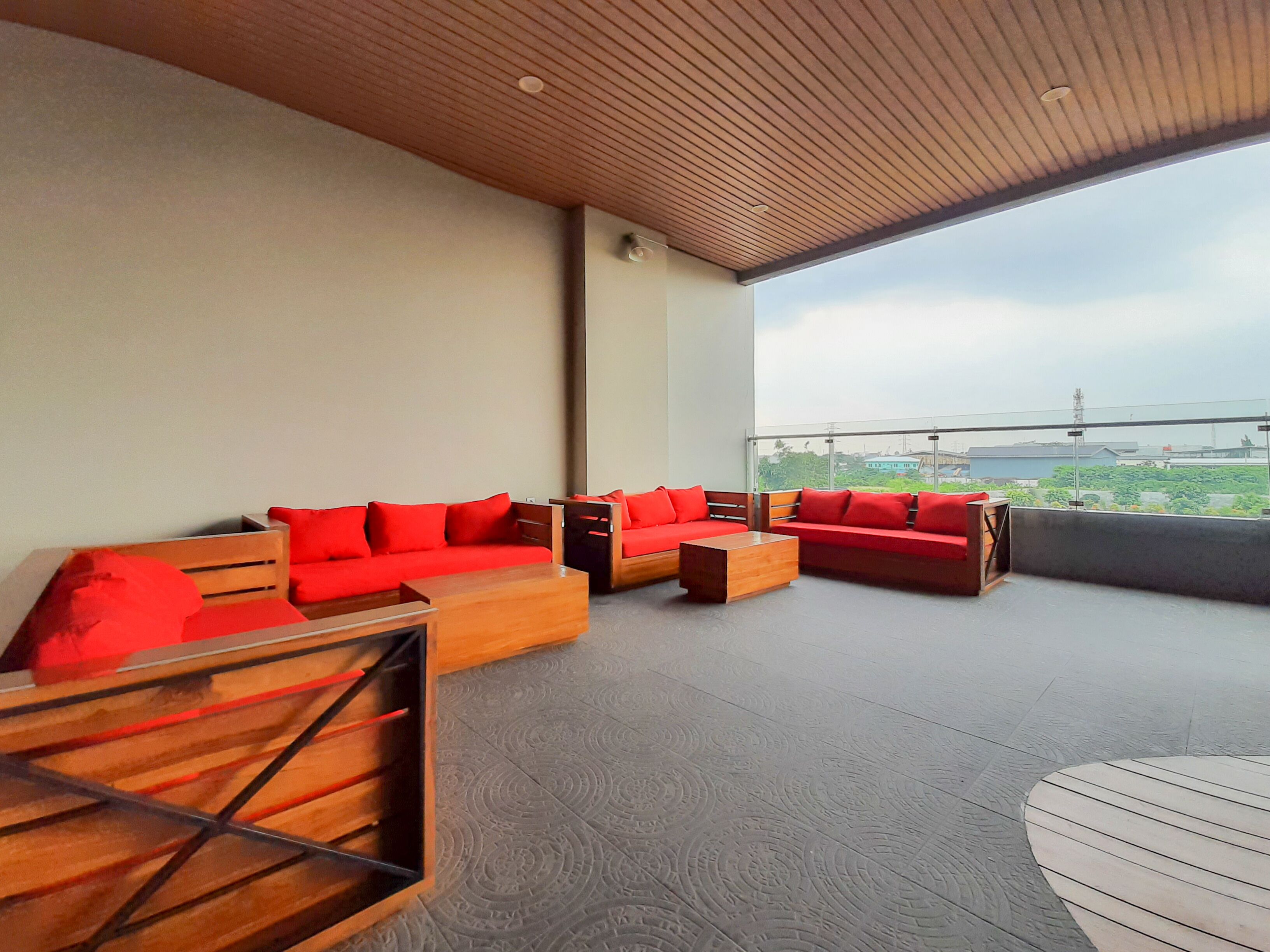 Un espacio al aire libre moderno con sofás rojos y mesas de madera, con un amplio ventanal y vistas a la ciudad.