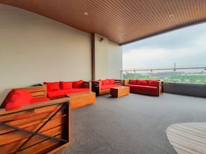 Un espacio al aire libre moderno con sofás rojos y mesas de madera, con un amplio ventanal y vistas a la ciudad.