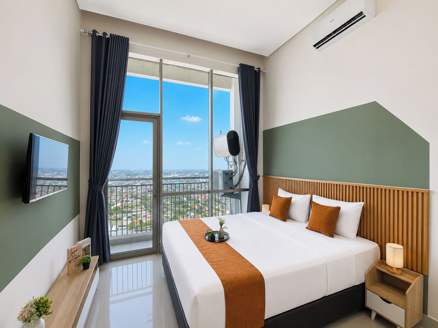Habitación de hotel con una cama grande, televisión, balcón con cortinas y vista a la ciudad.