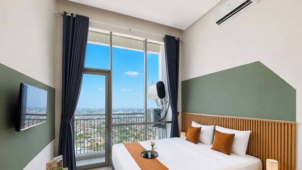 A hotel room with a large bed, a TV, a balcony with curtains, and a view of the city. - Nice Look Studio At Apartment Tamansari Iswara (Bekasi)
