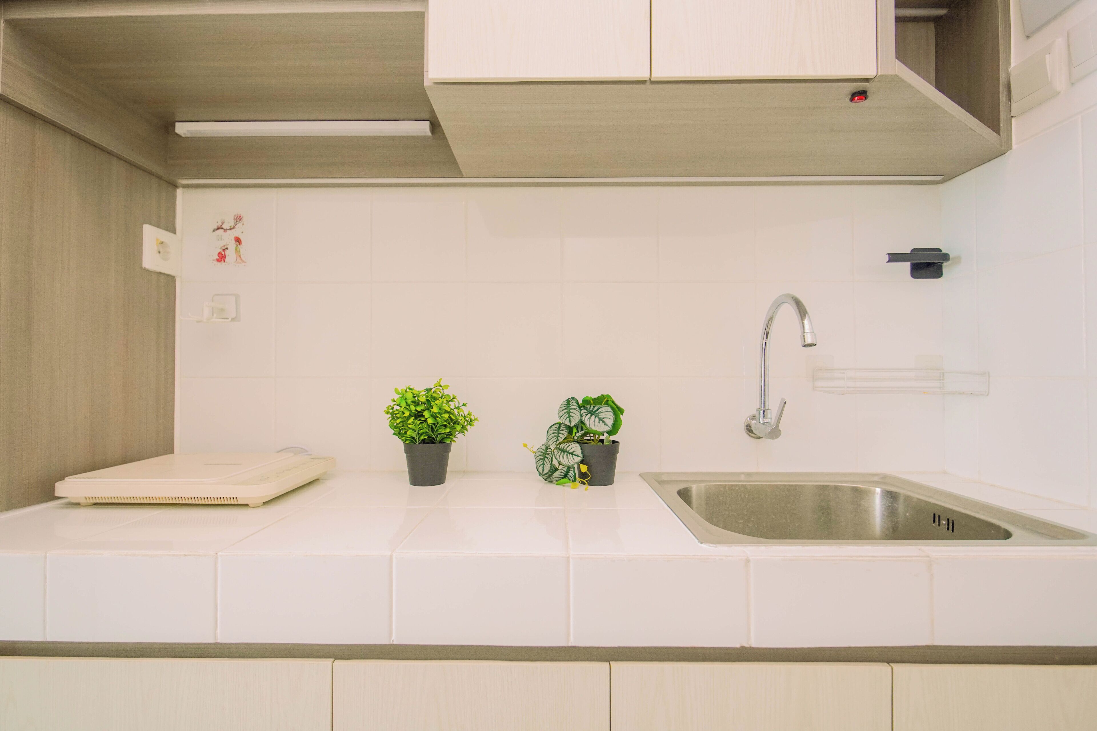 Een keuken met witte tegels, een roestvrijstalen spoelbak, een kraan en twee potplanten.