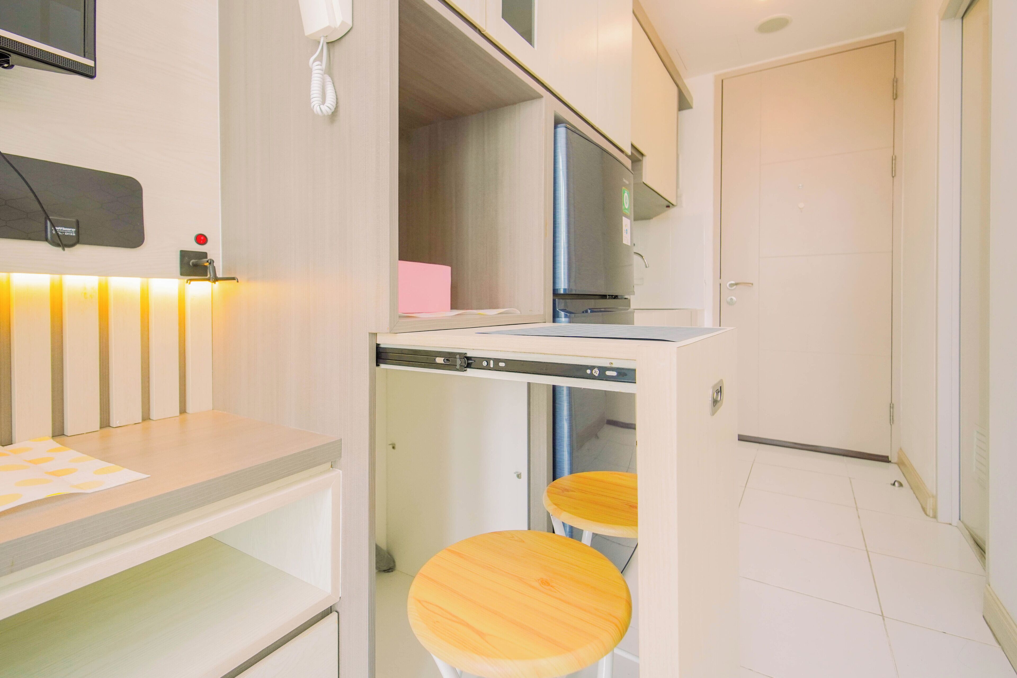 A compact hotel room with a kitchenette, a small dining table, and two stools.