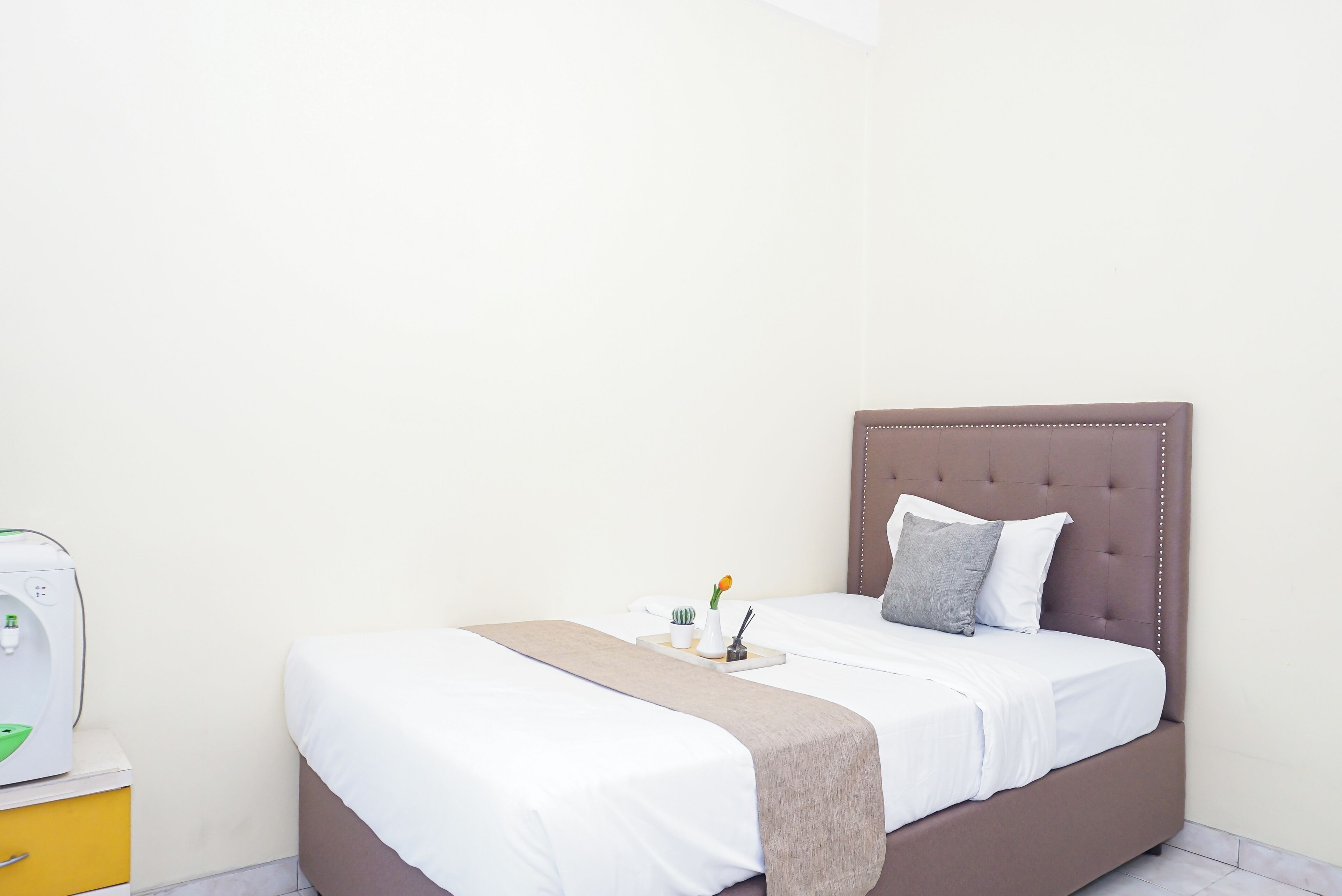 A neatly made bed with a brown headboard, white bedding, and a bedside table with a lamp and a small decorative item.