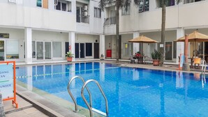 Una piscina con agua azul cristalina, rodeada por una terraza de azulejos. Hay sillas de descanso y sombrillas, y un cartel que indica la profundidad de la piscina.