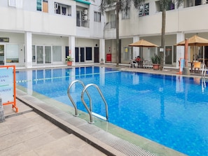 Ein Swimmingpool mit klarem, blauem Wasser, umgeben von einer gefliesten Liegefläche. Liegestühle und Sonnenschirme sind vorhanden, und ein Schild gibt die Wassertiefe an.