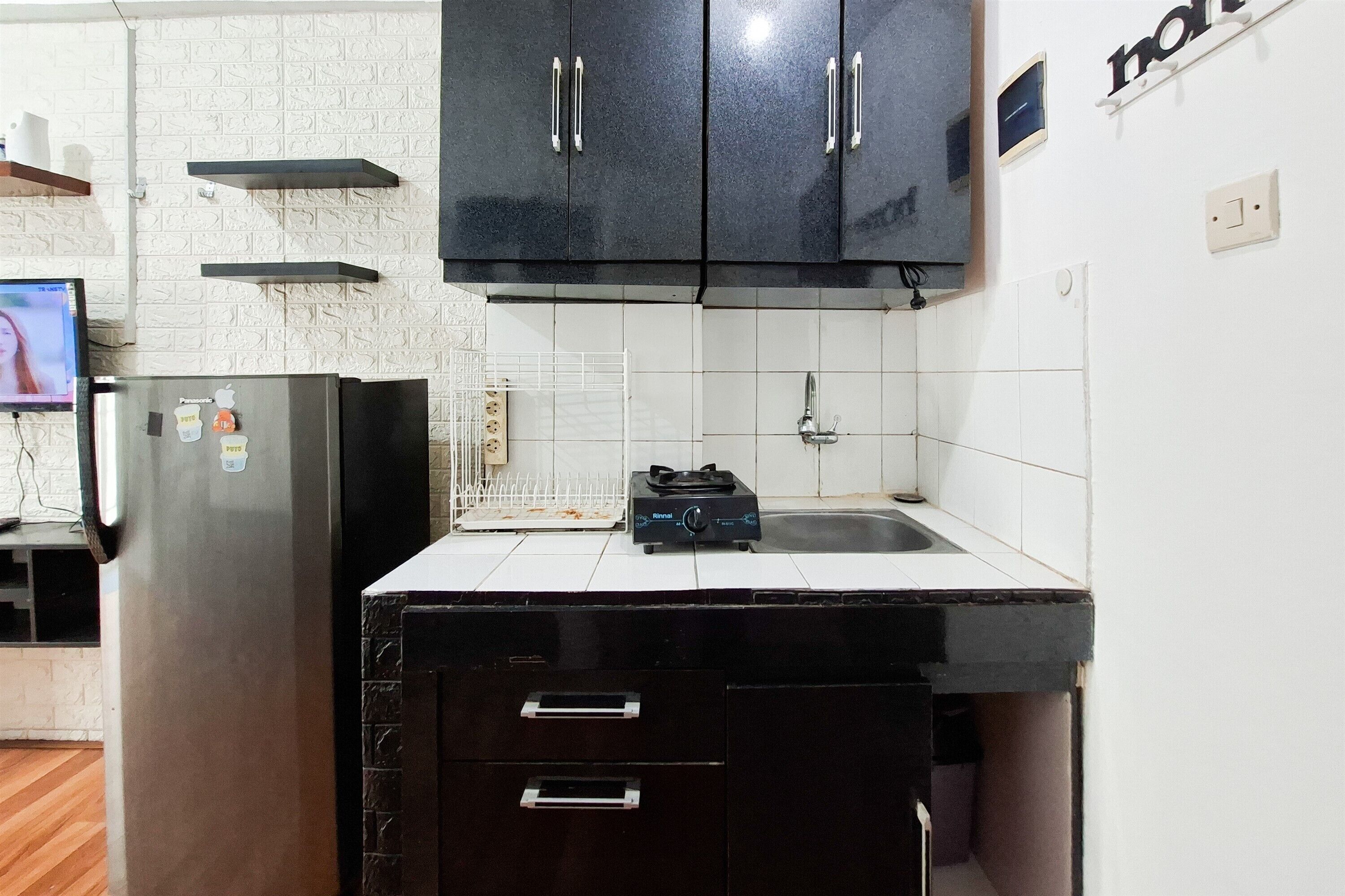 Eine Küche mit schwarzen Schränken, einer weißen Arbeitsplatte, einem Edelstahlkühlschrank und einer gefliesten Spritzschutzwand.