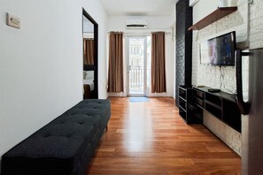 Un pasillo con un banco, un televisor y una zona de cocina con pared de ladrillo.