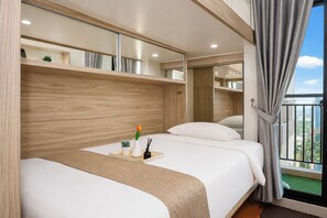 A hotel room with a bed, a bedside table with a vase and a plant, a mirror, and a view of the city through a window. - Homey And Warm Studio Room At Apartment Dave (Depok)