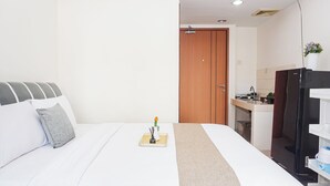 Een hotelkamer met een bed, een klein tafeltje met een vaas, een houten deur en een kitchenette.