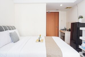 A hotel room with a bed, a small table with a vase, a wooden door, and a kitchenette area. - Comfortable Living In Studio Room At Apartment Margonda Residence 3 (Depok)